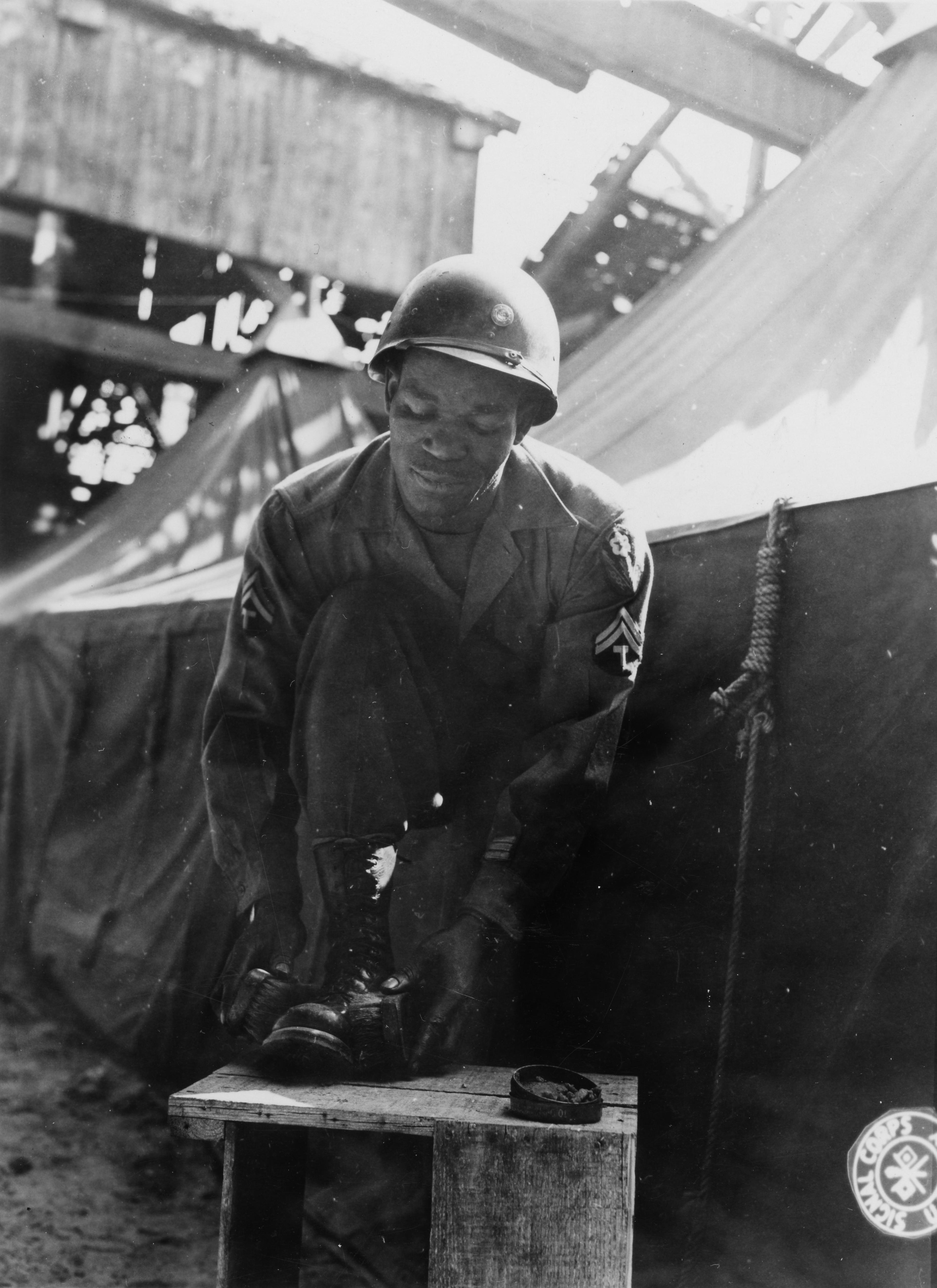 Historical image showing Before taking off on a pass, Corporal Clarence Carter, 1808 Bainbridge St. Philadelphia, Pa., with 411th Port Company, gives his shoes a good shine. of Black American soldiers during WWII