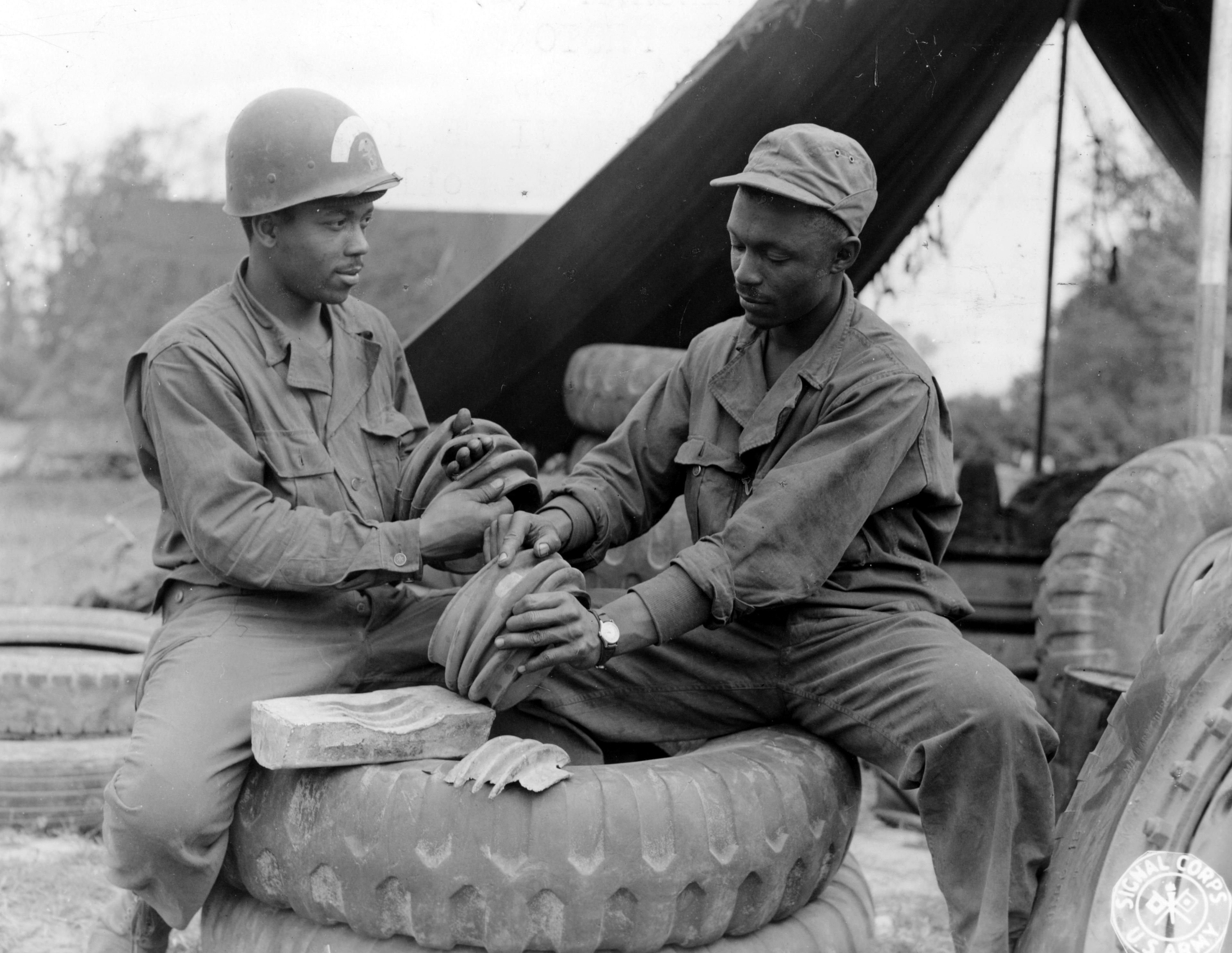 Historical image showing S/Sgt. William H. Holly and Sgt. Moses H. Mason repair a drive shaft housing using an improvised babbit mold. of Black American soldiers during WWII