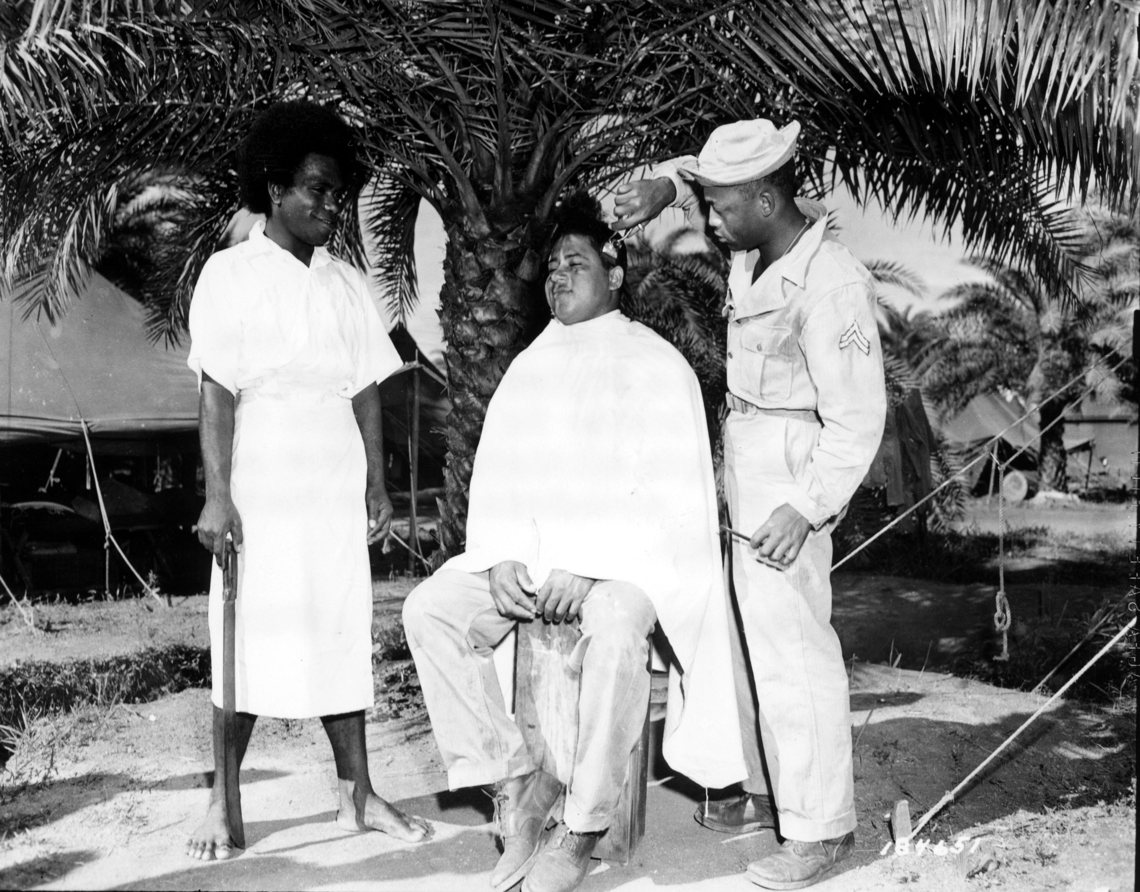 Historical image showing Sgt. Walter Rothschild of Birmingham, Ala., gets a "G.I." haircut while a Fijian native awaits his turn. of Black American soldiers during WWII