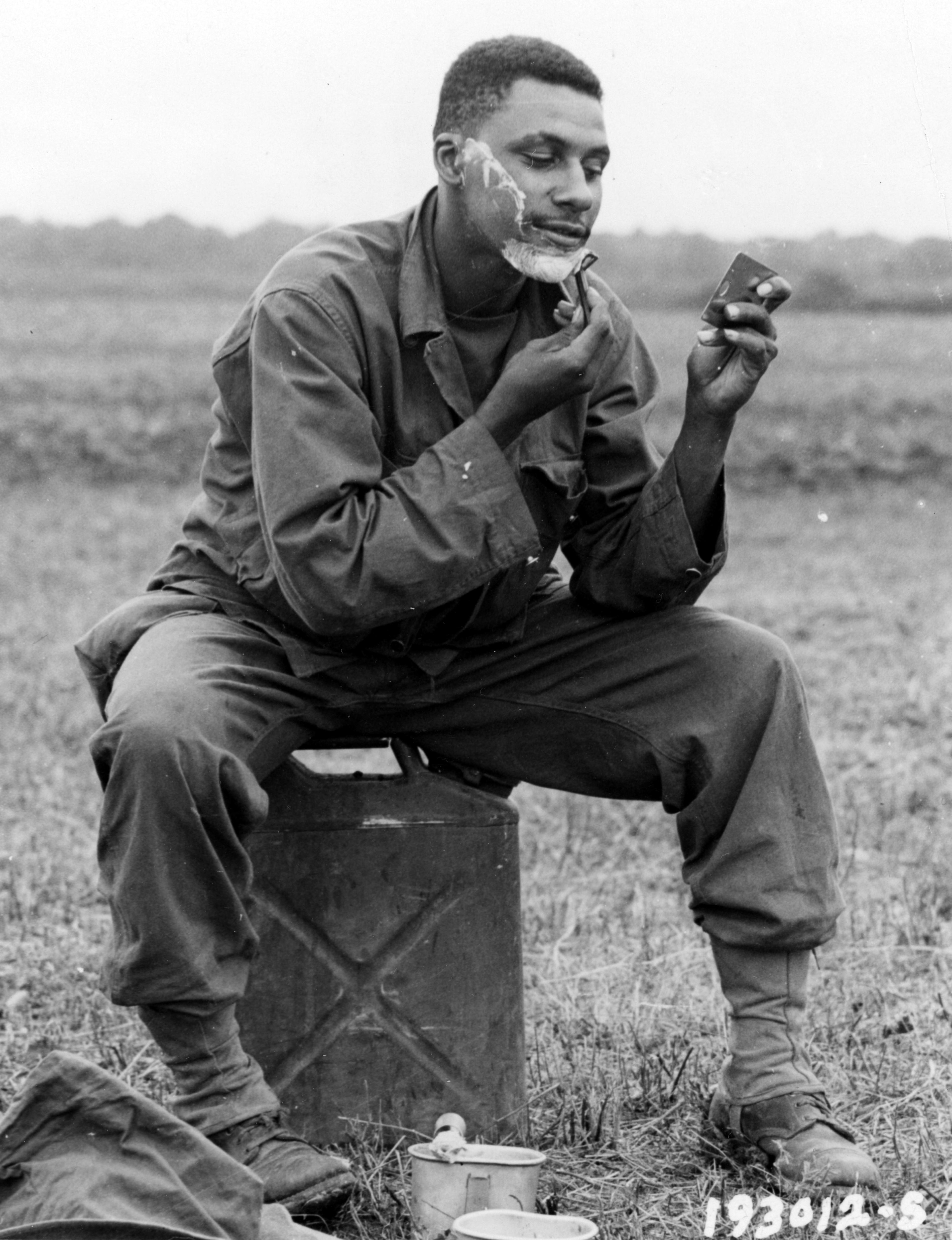 Historical image showing Corporal Edward W.P. Landrum takes time out to shave during a break in firing. of Black American soldiers during WWII
